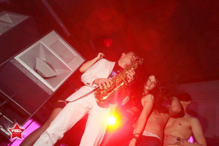 Performer plays saxophone under red stage lights