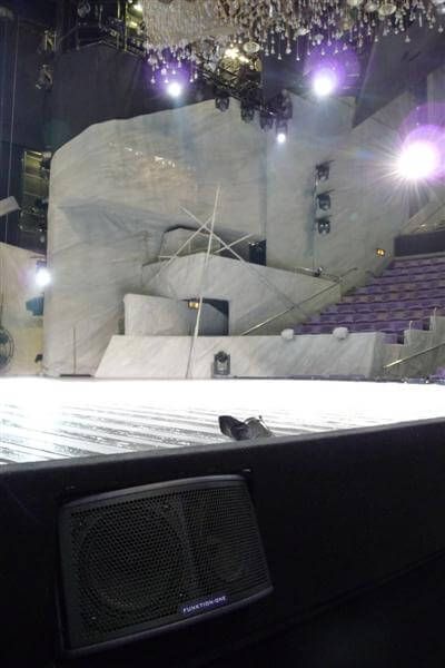 Funktion-One monitor at front of stage with dramatic lighting and stone-style set.