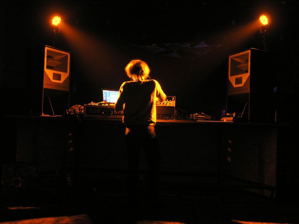 DJ performing under warm lighting with two Funktion-One speakers flanking the booth.