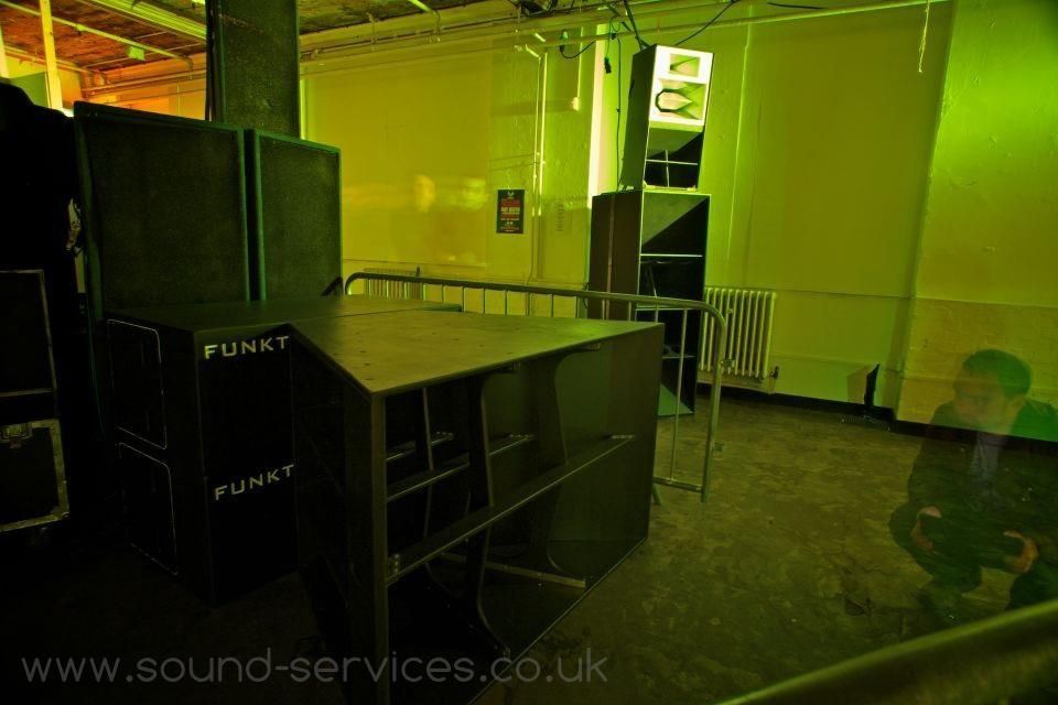 Funktion-One bass speakers and stacks in a dimly lit green indoor venue.