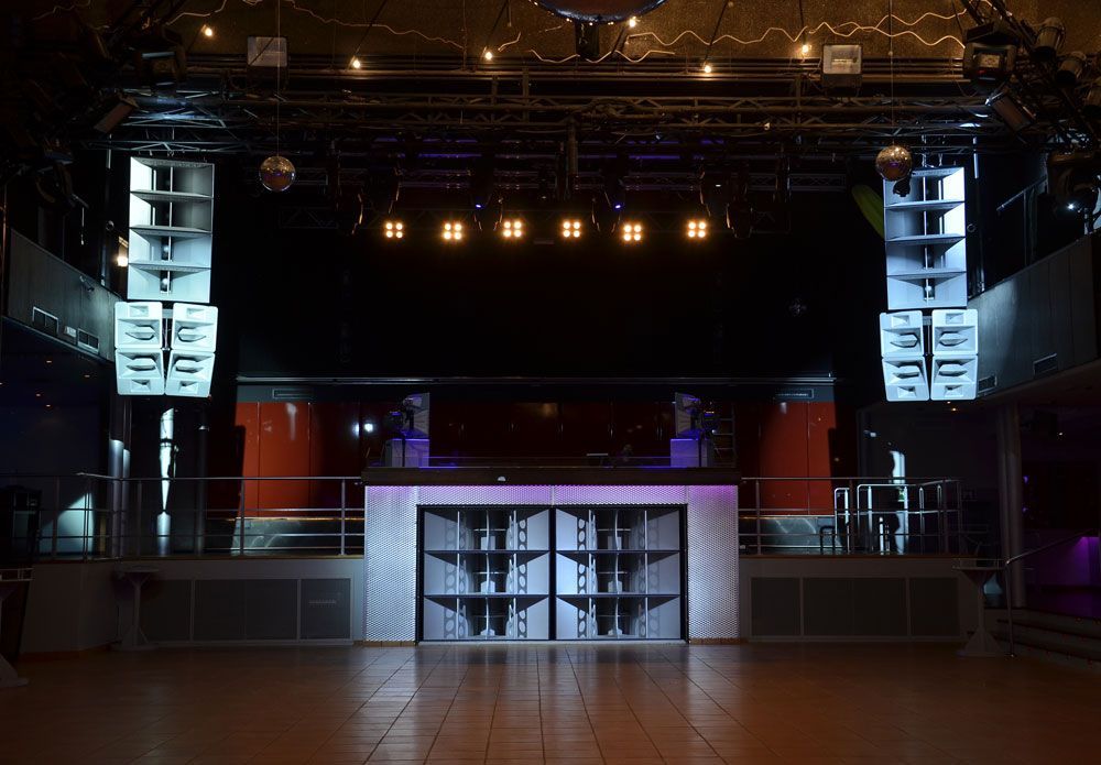Empty nightclub with Funktion-One speaker stacks and illuminated DJ booth.