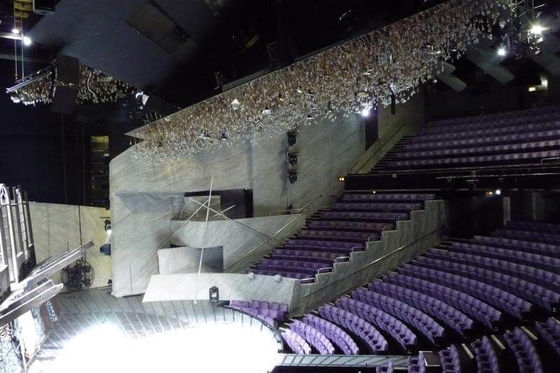 Purple auditorium with angled seating, concrete textures, and suspended lighting above stage.