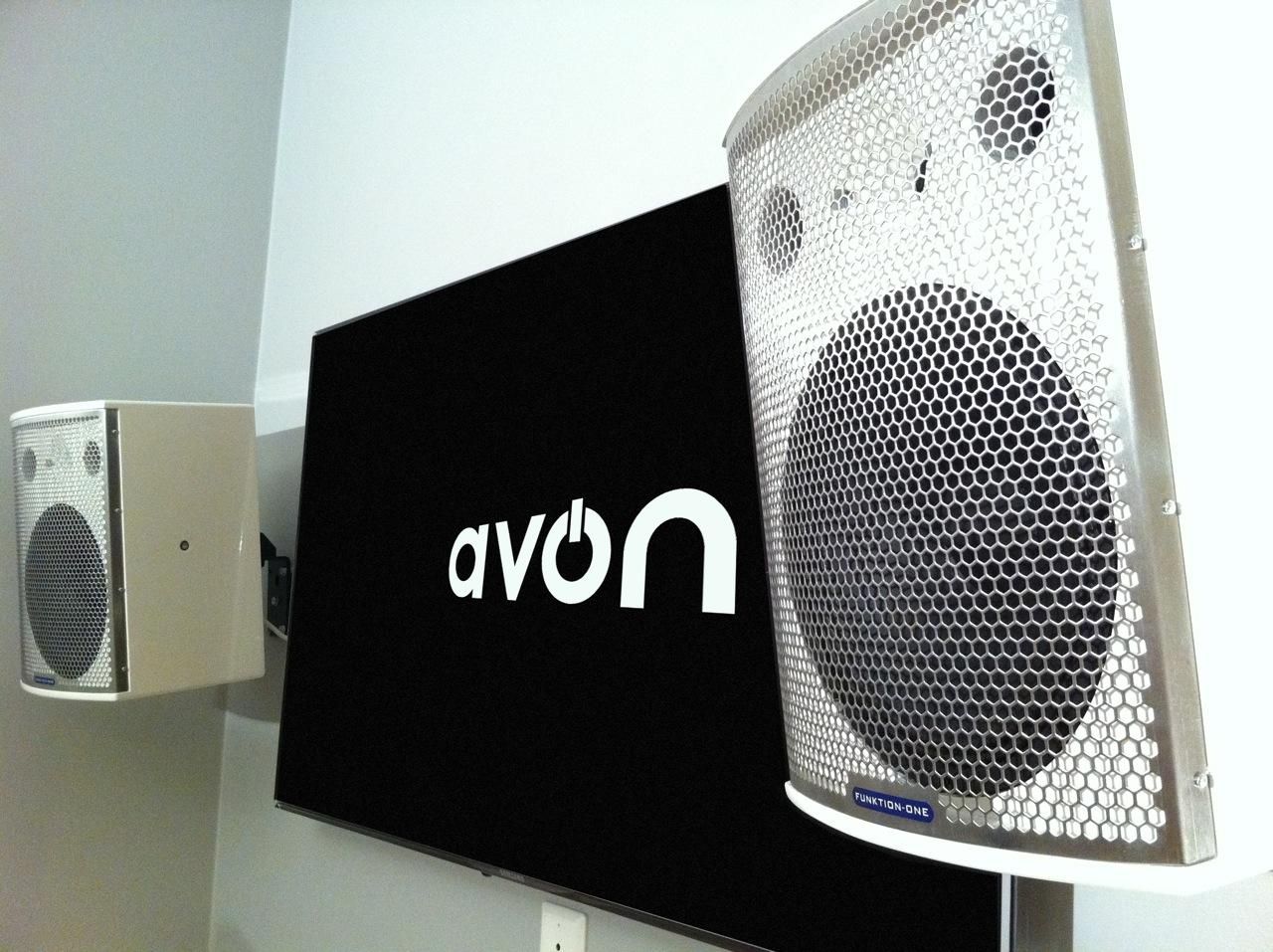 Funktion-One wall-mounted speakers beside a screen displaying the AVON logo.