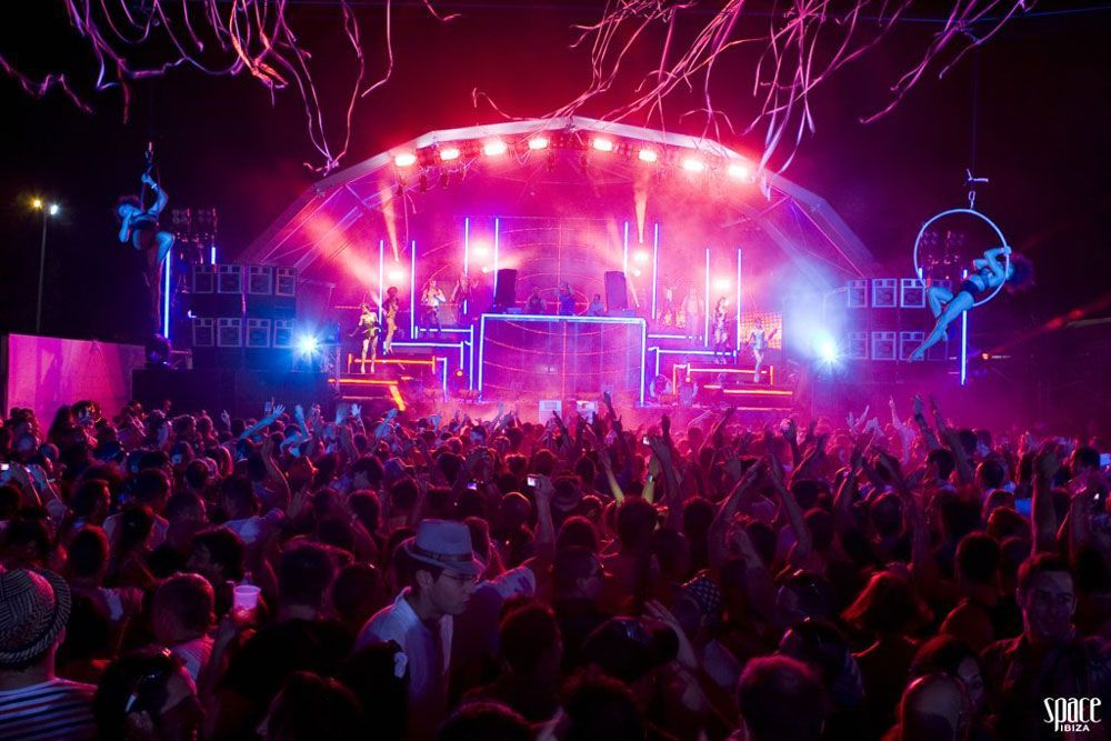 Crowd and stage with aerial performers and lighting effects at a night music festival.