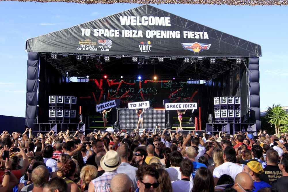 Crowd gathered in front of stage at Space Ibiza Opening Fiesta with large speaker stacks.
