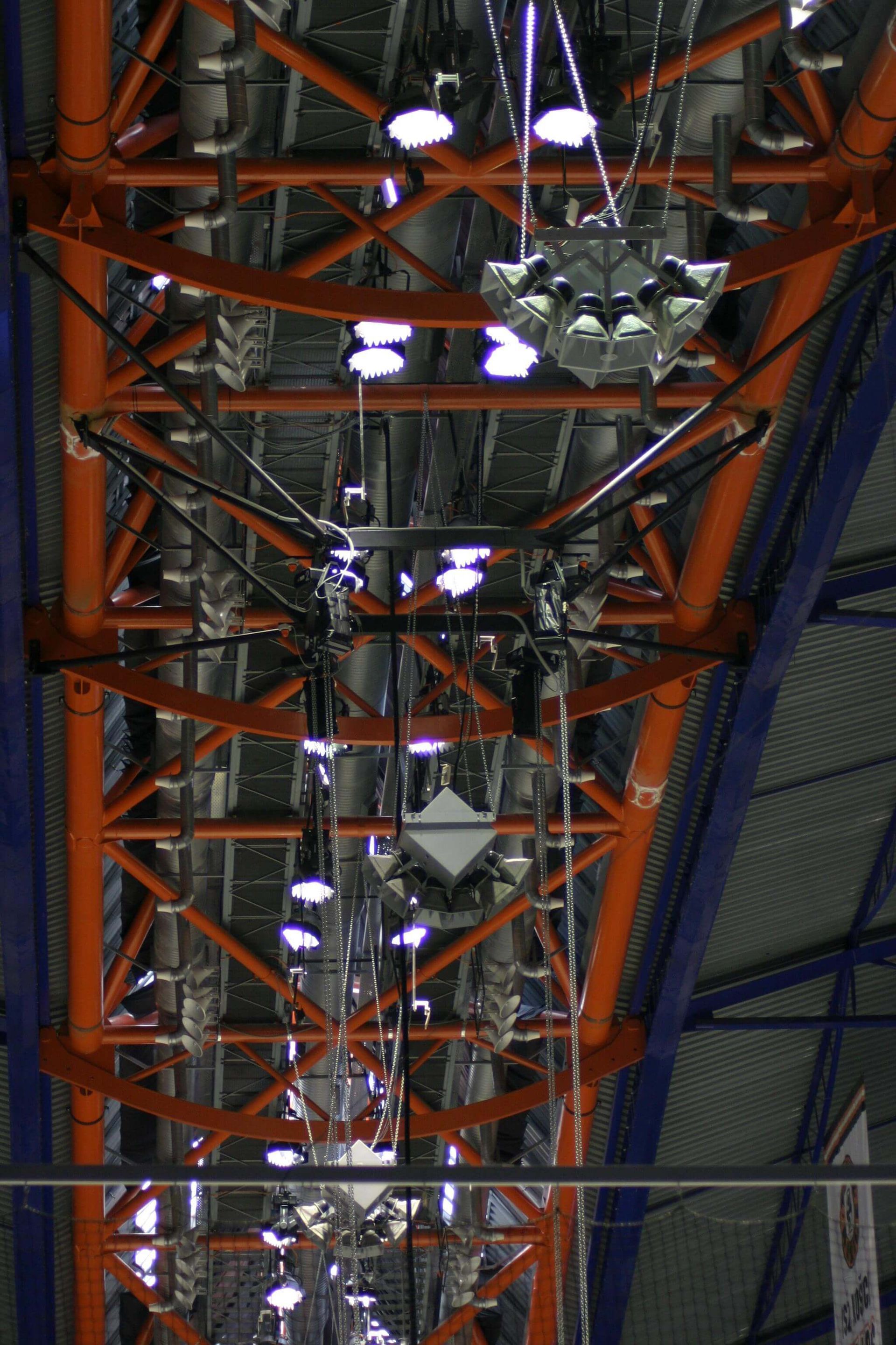 Orange metal beams and industrial lighting form a geometric pattern on a large ceiling. 