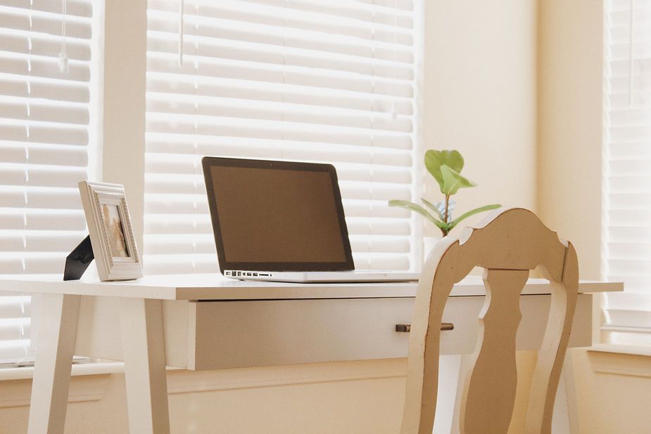 A laptop computer is sitting on a white desk in front of a window.