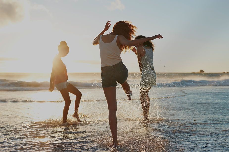 Three women are dancing on the beach at sunset.