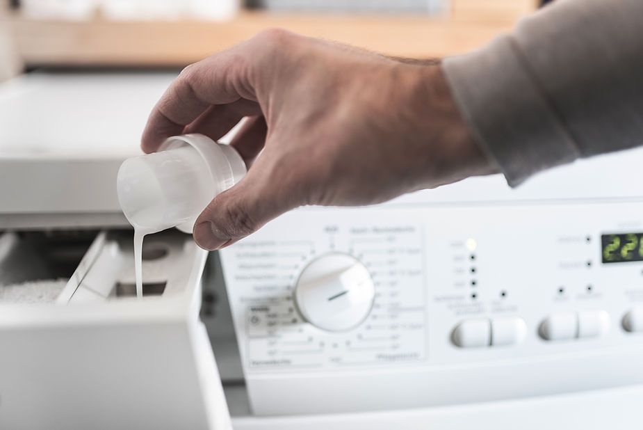 A person is pouring liquid into a washing machine.