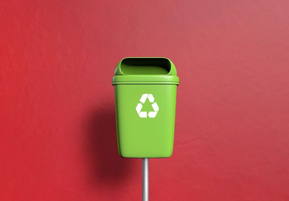 A green trash can with a recycling symbol on it is on a pole.
