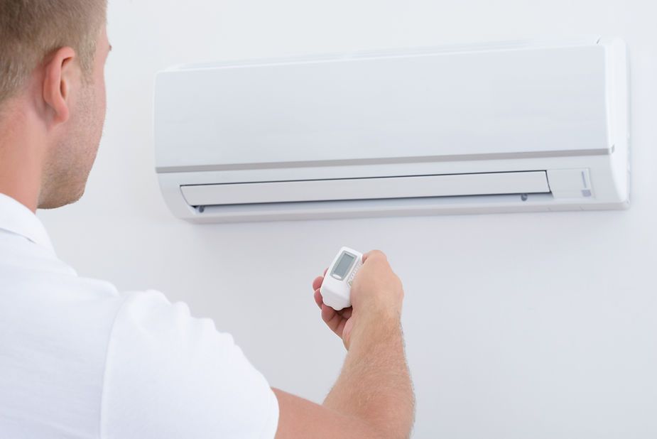 A man is using a remote control to turn on an air conditioner.