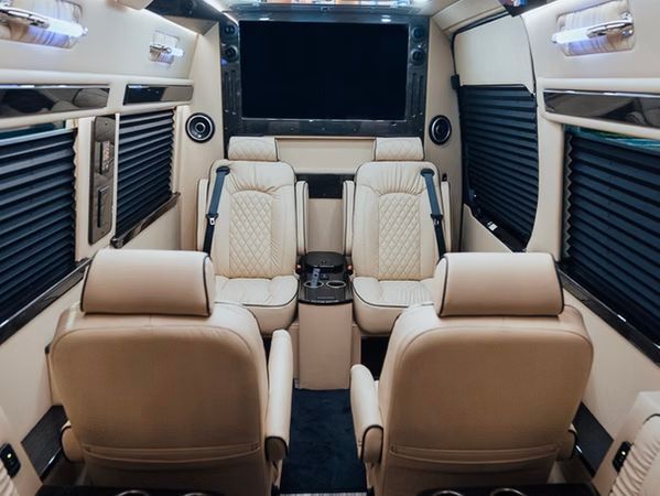 Luxurious van interior with beige leather seats, large TV, and dark blinds.