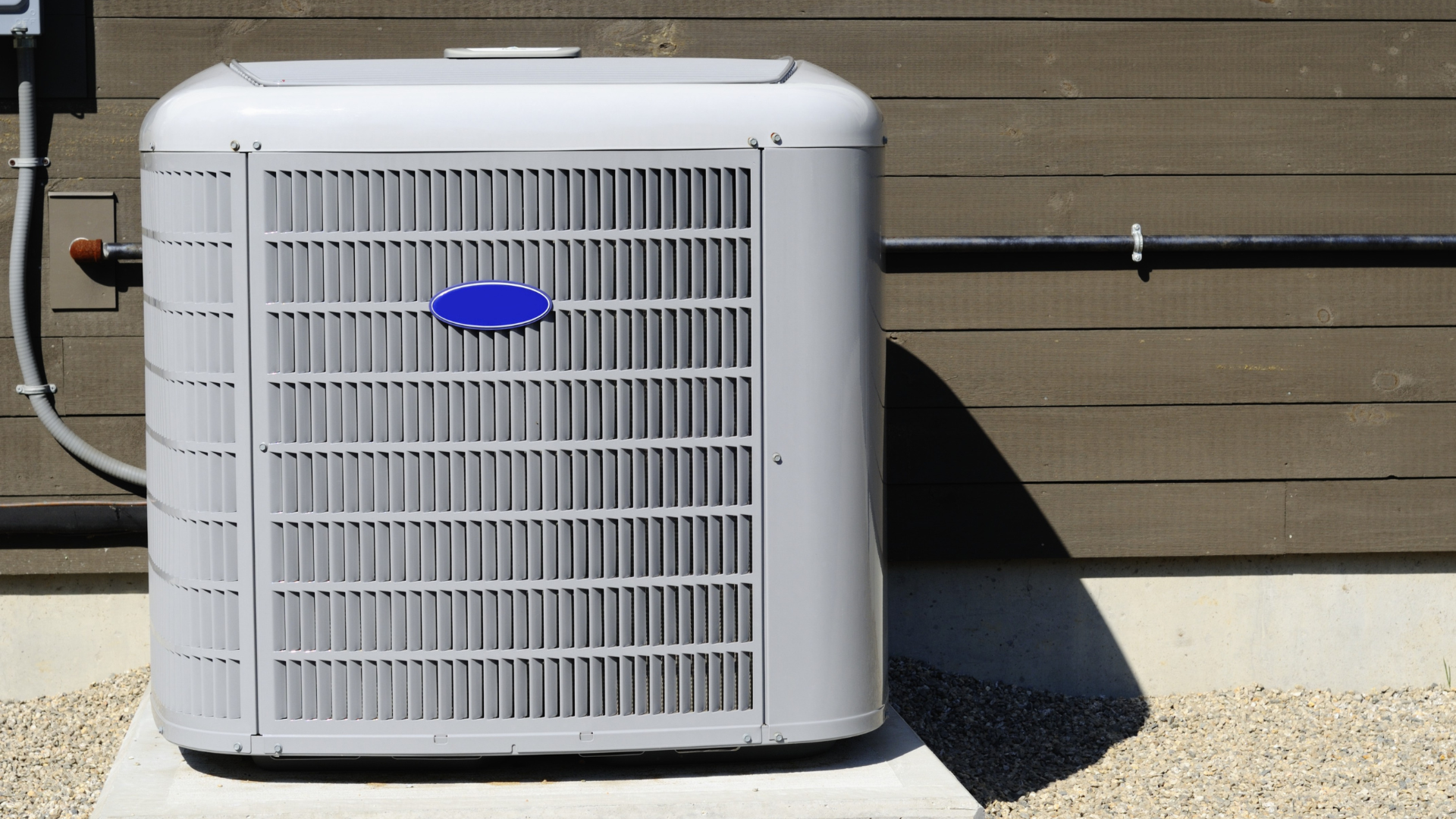 Air conditioner unit outside a building with gray siding and gravel.