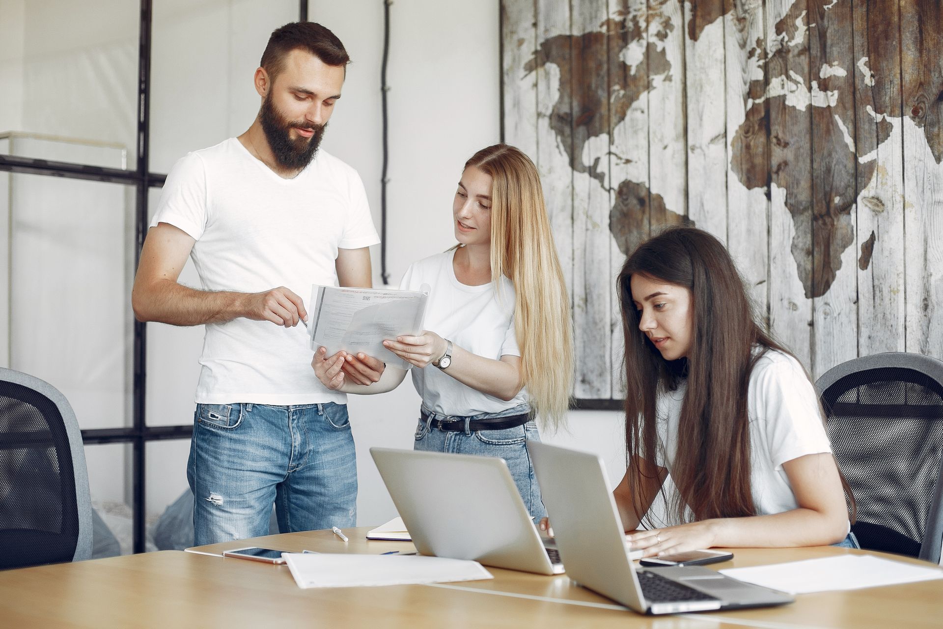 Drie mensen in een modern kantoor bekijken papieren en laptops, één van hen wijst.