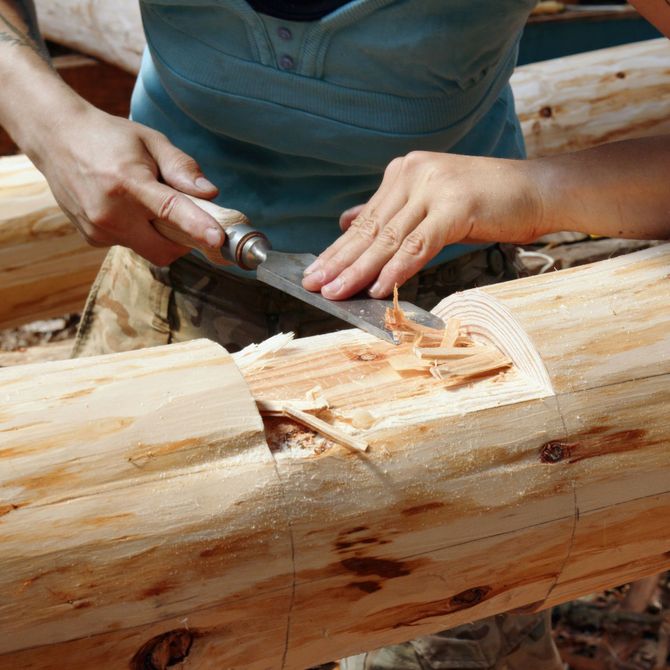 Person carving a wooden log with a chisel, creating a notch in the timber.