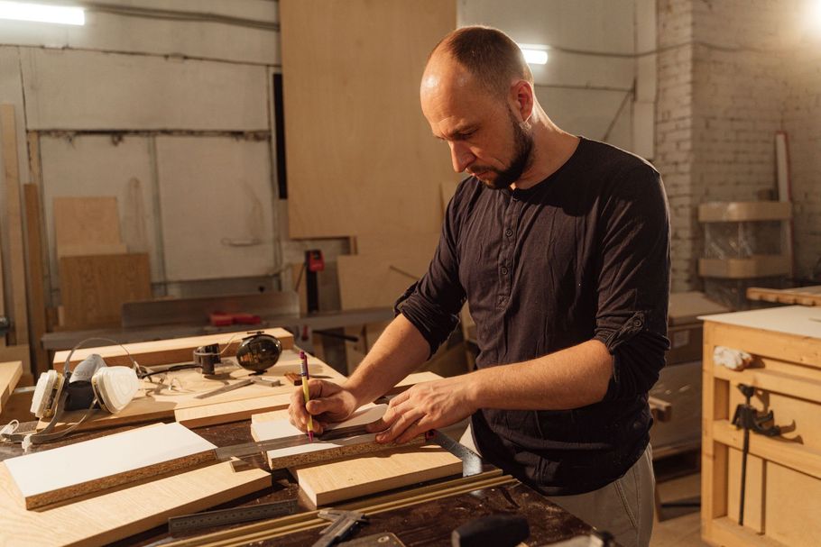 Man working in a woodshop, using a hand tool on a wooden board at a workbench.