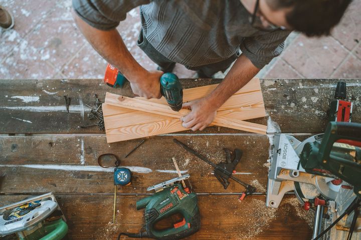 Person using a drill to assemble wood on a workbench with tools scattered around
