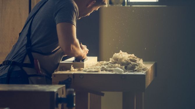 Person kneading dough on a flour-dusted table in a dim workshop, with a bowl nearby