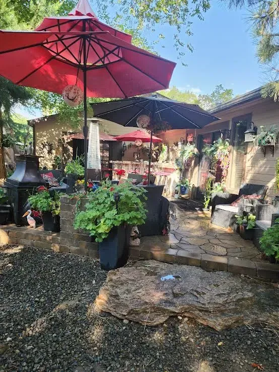 Red and black patio umbrellas shade a brick patio filled with potted plants and seating.