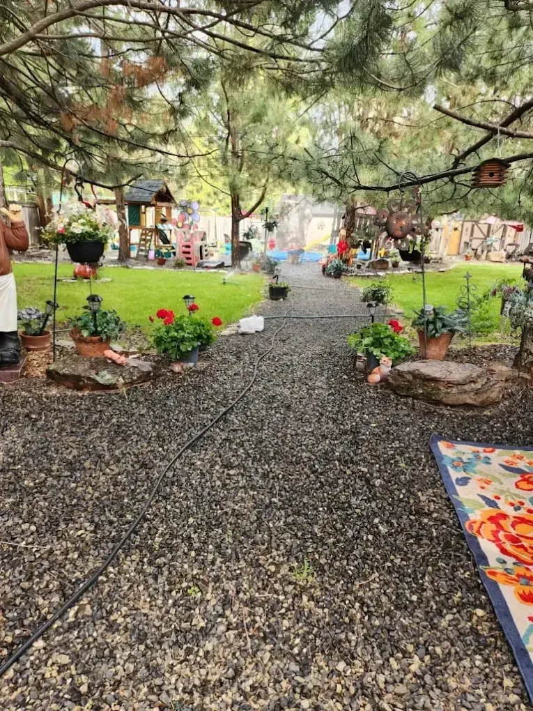 Gravel path through a garden with flower pots, green lawns, and a play structure in the background.