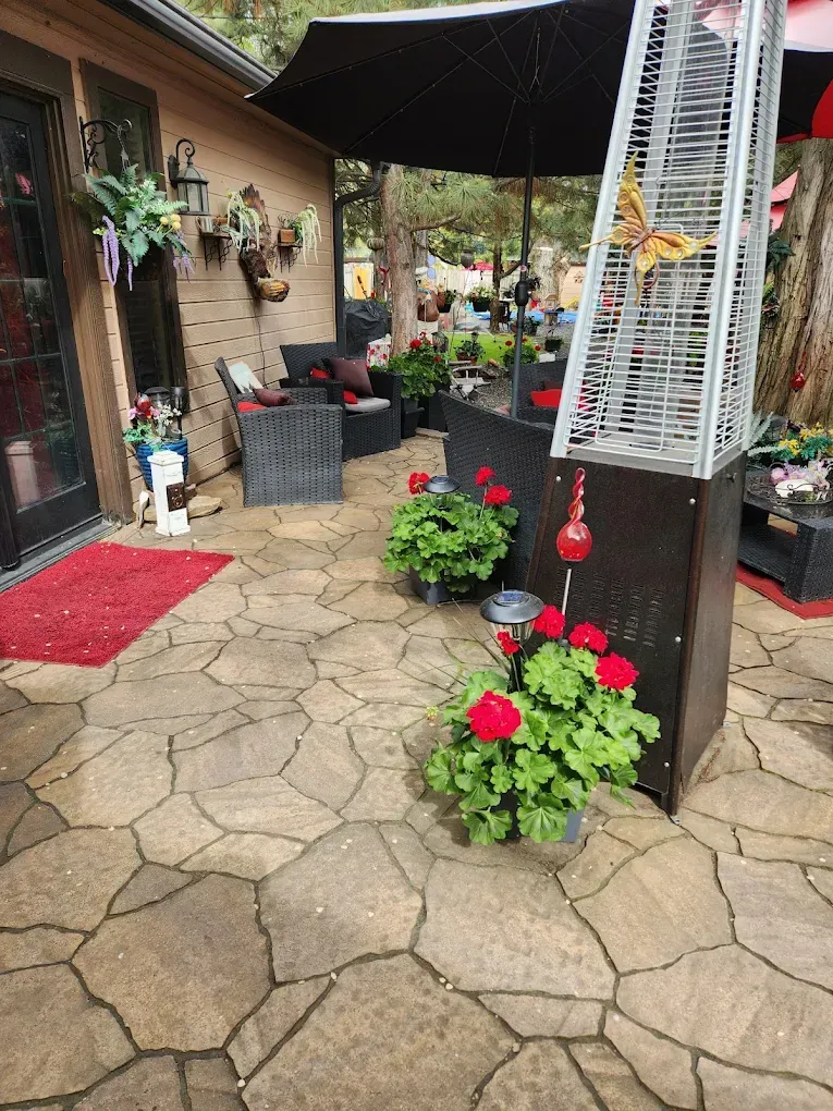 Patio with stone floor, black umbrella, outdoor heater, red geraniums, and patio furniture.