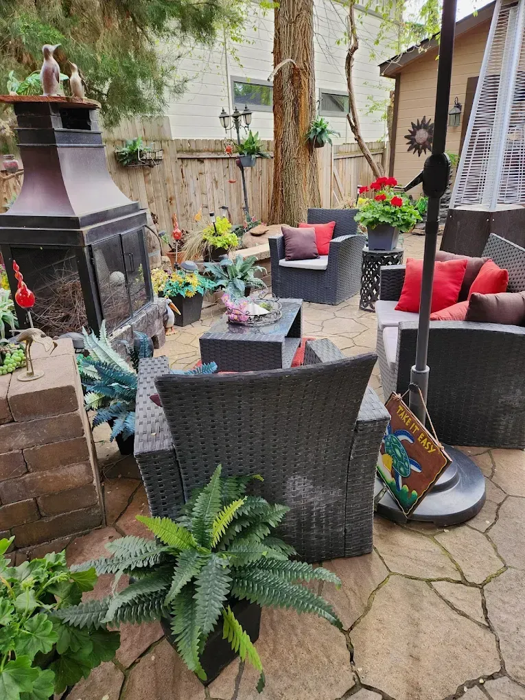 Patio with dark wicker furniture, fireplace, and potted plants on a stone surface.