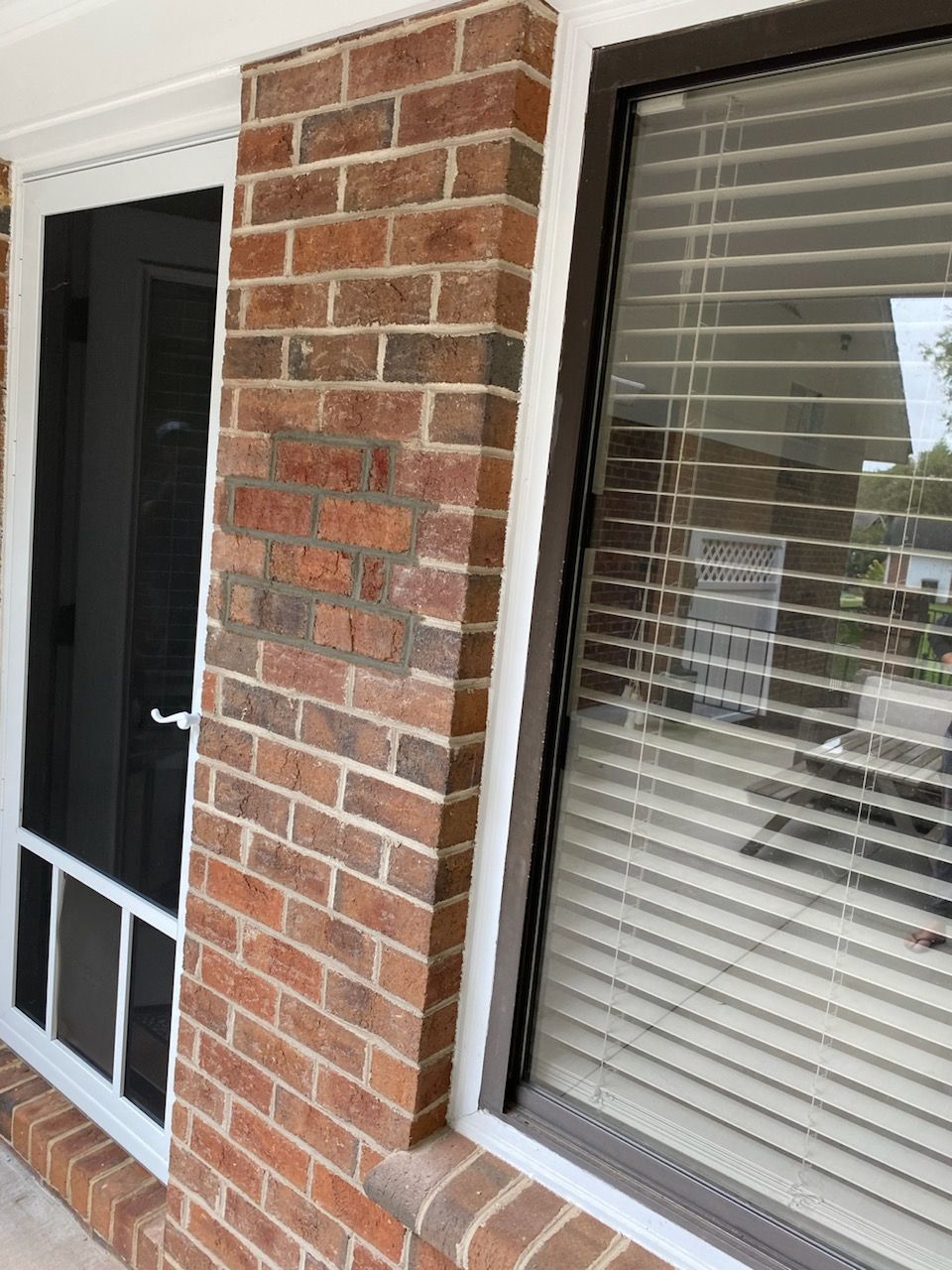 Brick facade with white-framed screen door and window with closed blinds.