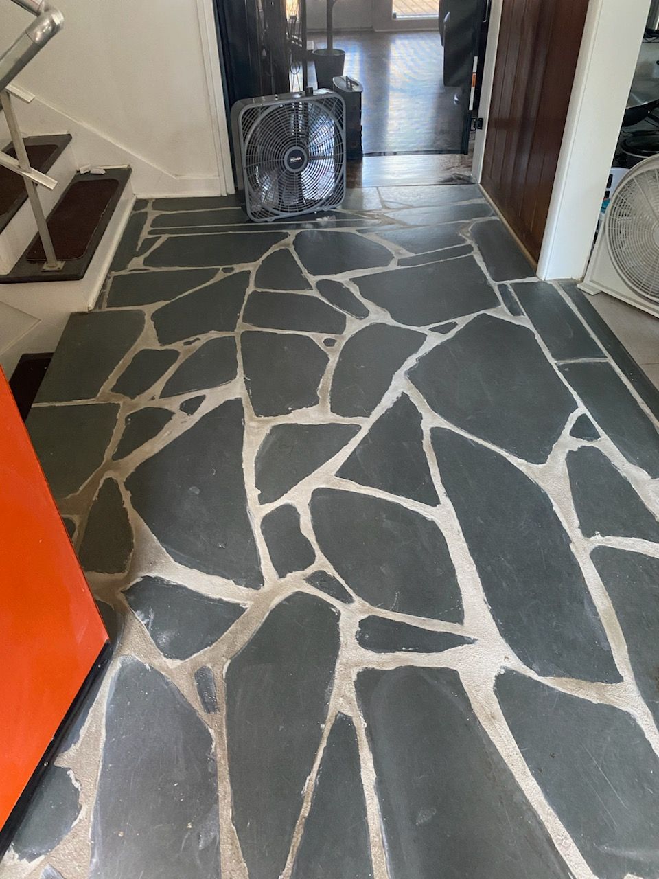 Dark gray flagstone tile entryway with a staircase and an orange door.