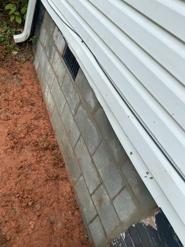 Exterior view of a house with white siding and gray cinder block foundation. Earth surrounds the foundation.