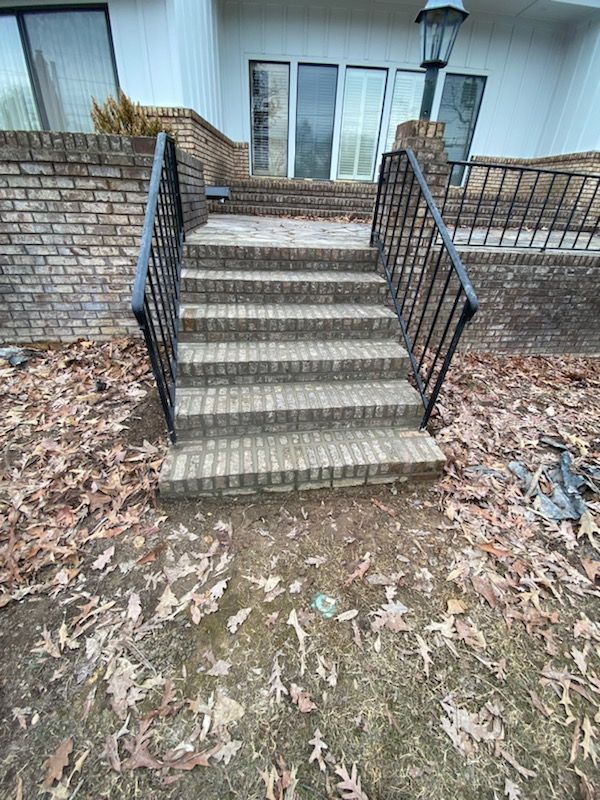 Brick steps with black railings leading up to a house entrance. Ground covered in fallen leaves.