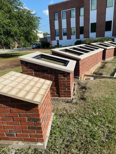 Brick structures with glass tops in a grassy area, in front of a building with a brick facade.