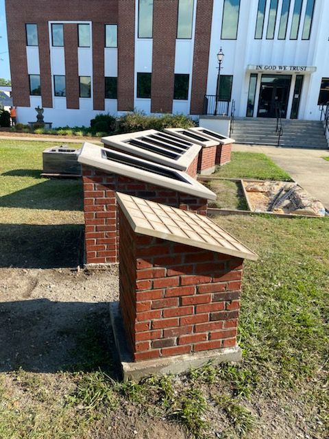 Brick structures with angled roofs in front of a building with large windows and steps.