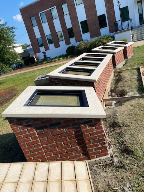 Brick structures with rectangular skylights, set in grass, in front of a brick building.