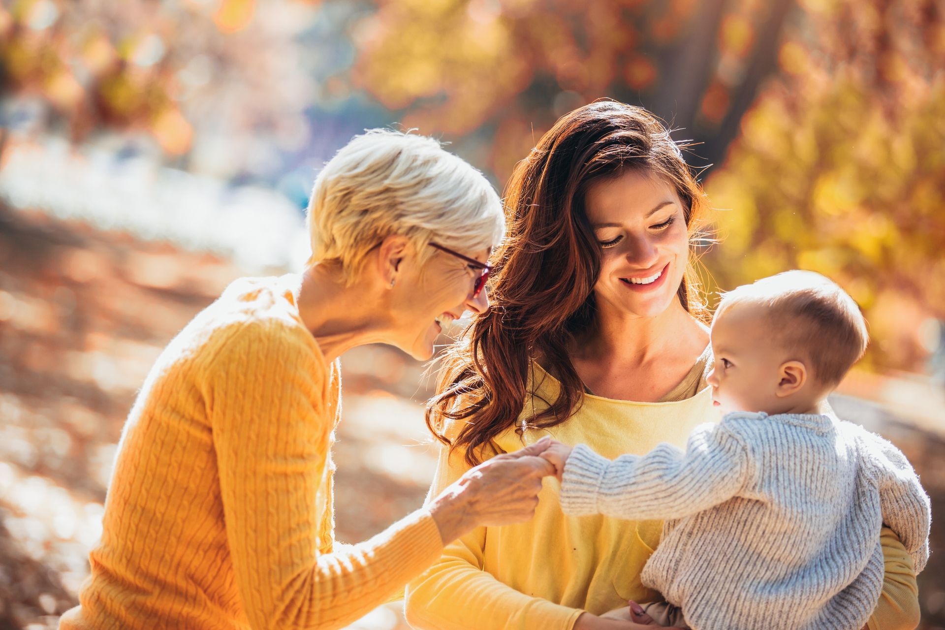 Two women are holding a baby in a park.