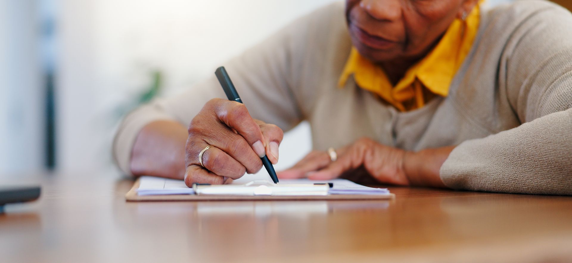 An elderly woman is writing on a clipboard with a pen.