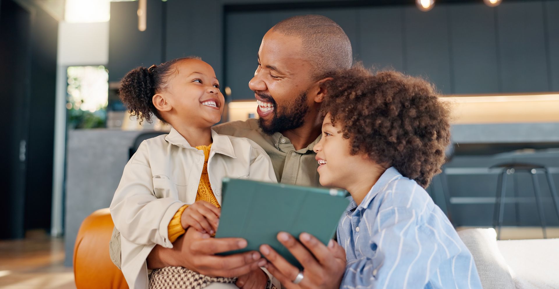 A man and two children are sitting on a couch looking at a tablet.