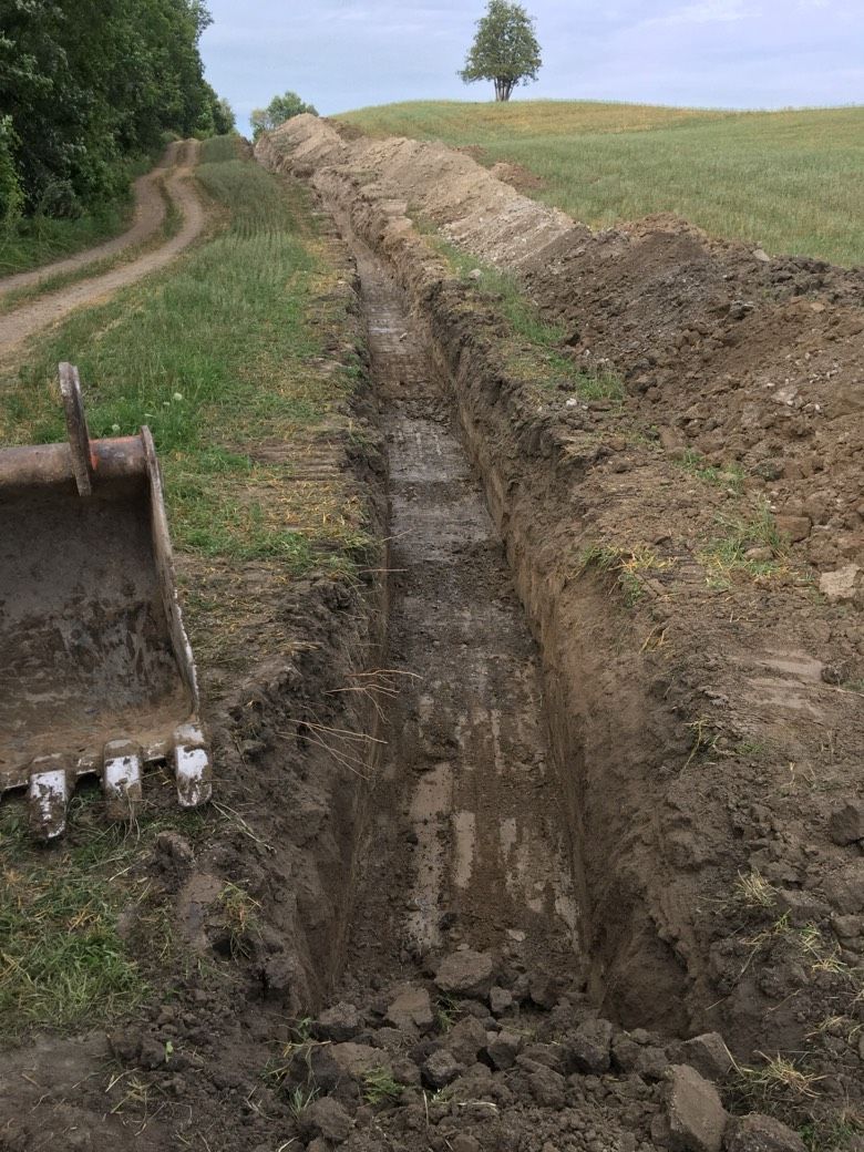 A bulldozer is digging a trench in a field next to a dirt road.