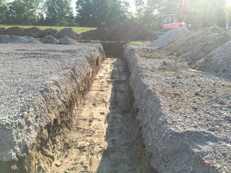 A trench is being dug in the dirt near a pile of gravel
