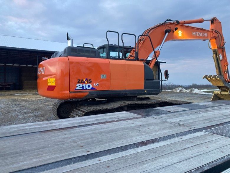 A large orange excavator is parked on a wooden platform.