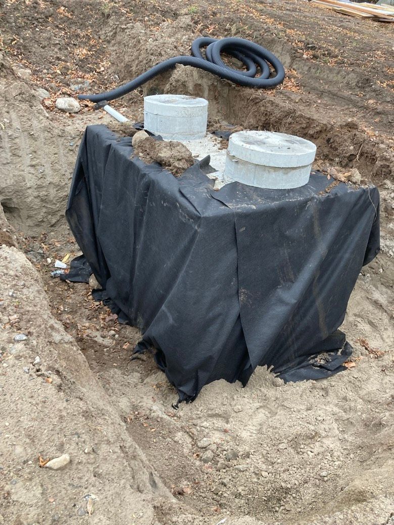 A septic tank is sitting in the dirt next to a hose.