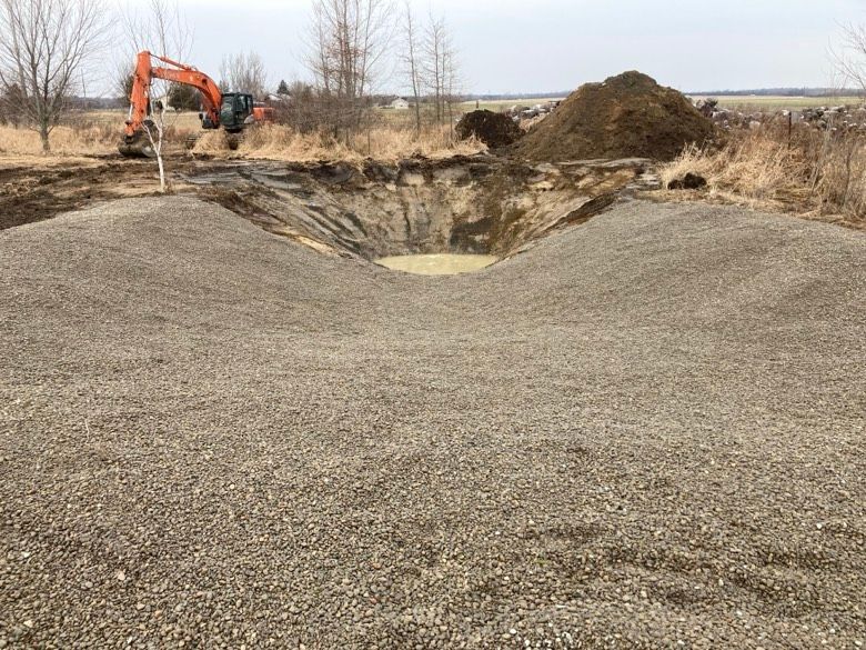 An excavator is digging a hole in the ground next to a pile of gravel.