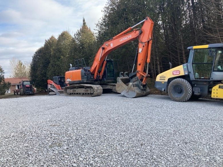 A group of construction vehicles are parked in a gravel lot.