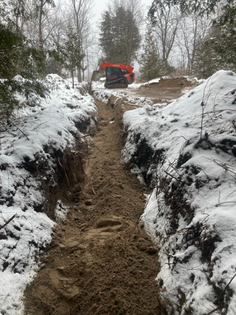 An excavator is digging a trench in the snow.