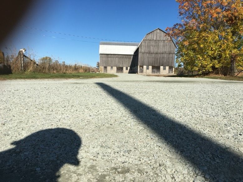 A person 's shadow is cast on the ground in front of a barn.