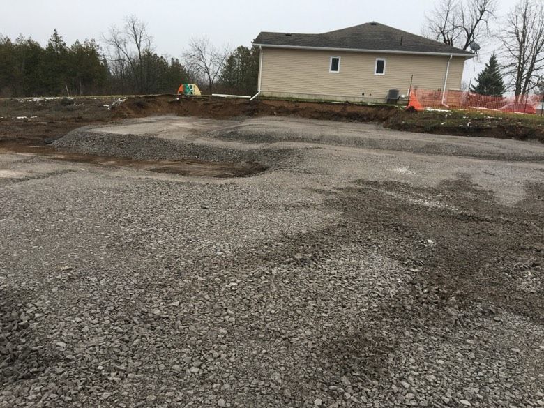A large gravel lot with a house in the background.