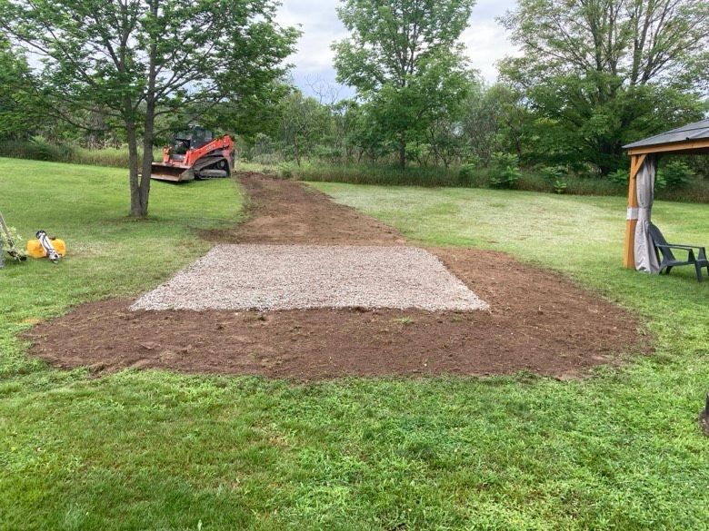 A tractor is driving down a dirt road in a grassy field next to a gazebo.