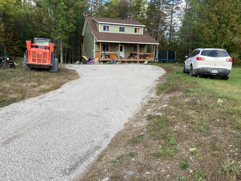 A car is parked on the side of a gravel road in front of a house.