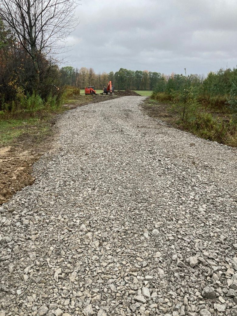 A gravel road going through a field with trees on both sides.