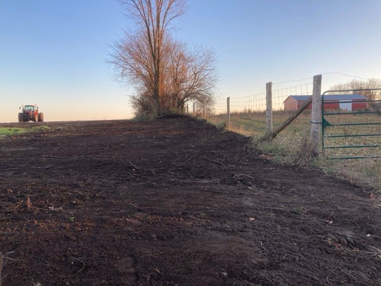 A tractor is driving down a dirt road next to a fence.