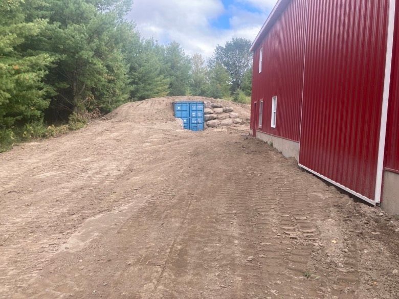 A red barn is sitting on top of a dirt hill next to a dirt road.